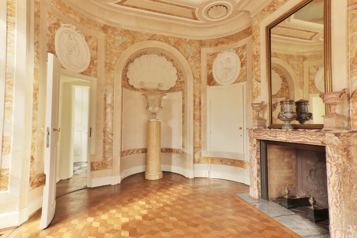 Łazienka w Pałacu Myślewickim, po prawej stronie znajduje się kominek, na którym wisi lustro, na kominu stoją wazy.
