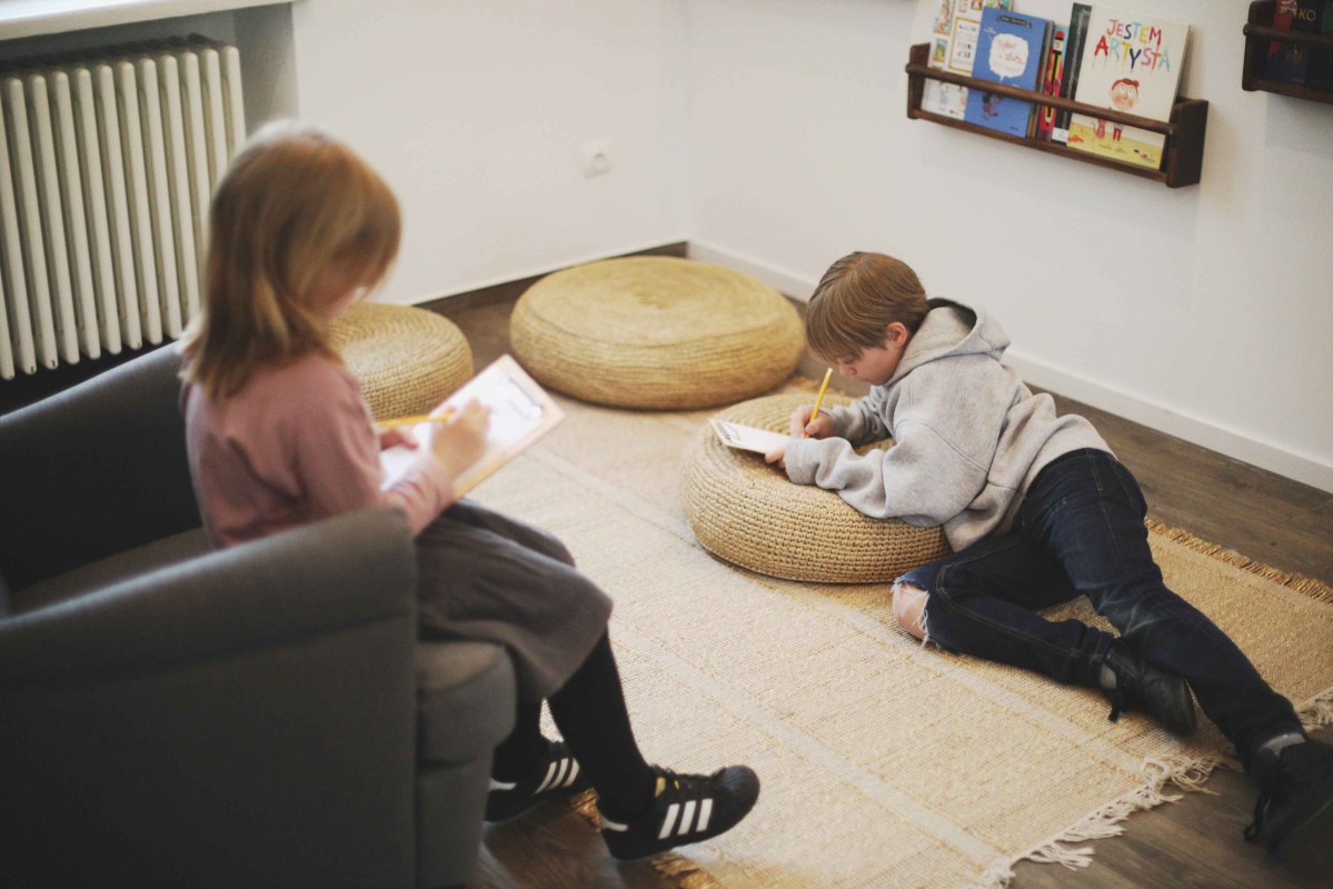Dziewczyna siedzi na fotelu, chłopiec leży na podłodze. Oboje trzymają w rękach książki.