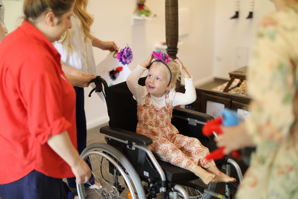 Dziecko na wózku dla niepełnosprawnych. Obok stoi opiekunka. 
