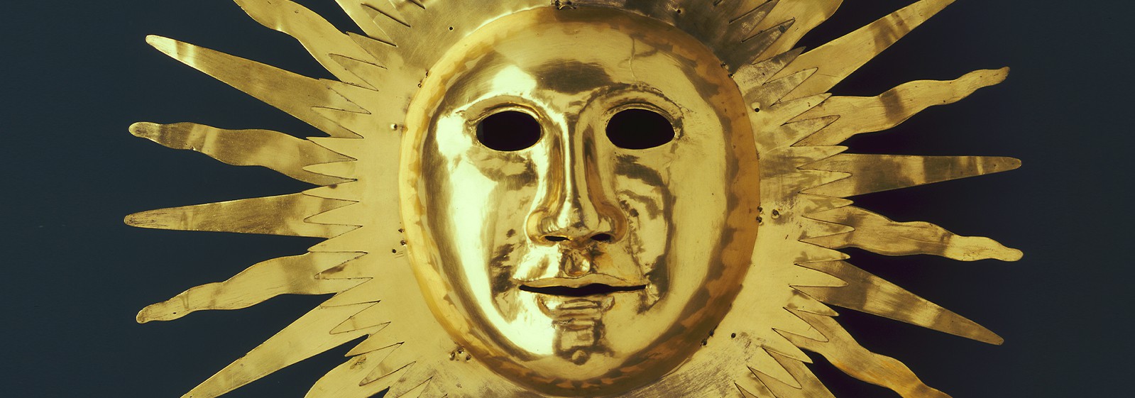 Złota maska słońce z podobizną króla Augusta II przedstawiona na granatowym tle. 