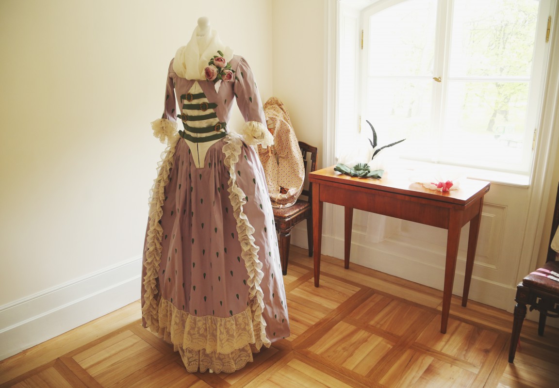Pokój, w którym stoi manekin z suknią z epoki oraz stolik.