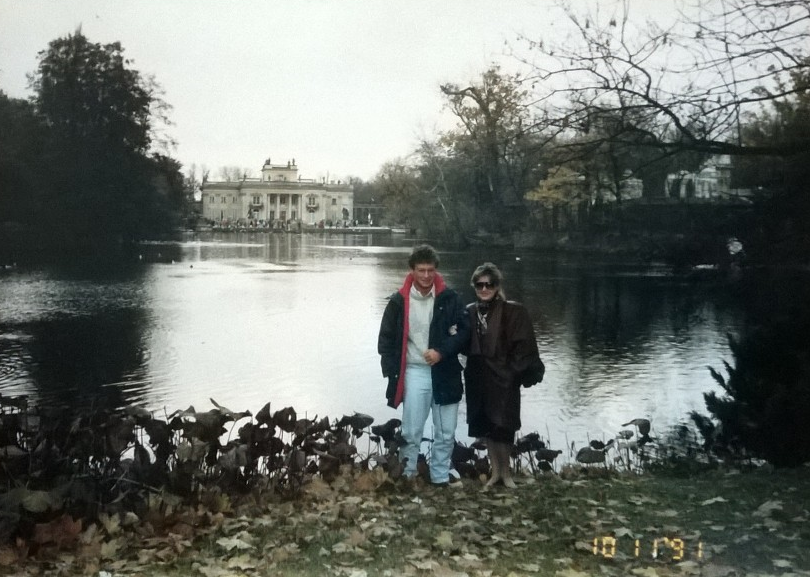 Mężczyzna i kobieta stoją nad wodą, w tle widać Pałac na Wyspie.