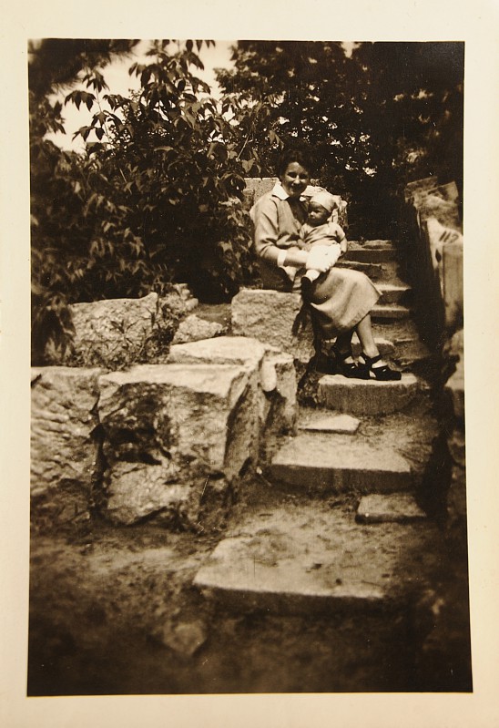 Kobieta siedząca na schodach trzyma na kolanach małe dziecko. 