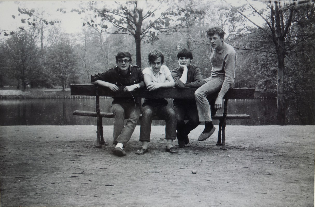 Grupa chłopców siedzi na ławce stojącej przy stawie.
