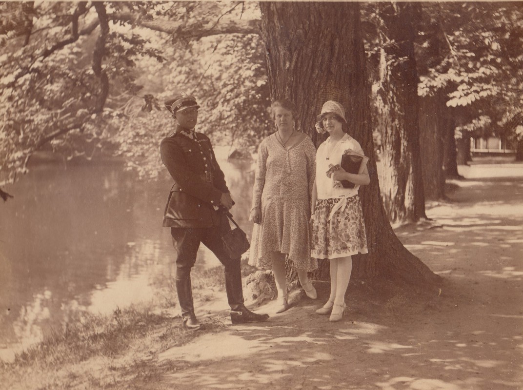 Mężczyzna w mundurze wojskowym i dwie kobiety stoją pod drzewem w łazienkowskim ogrodzie.