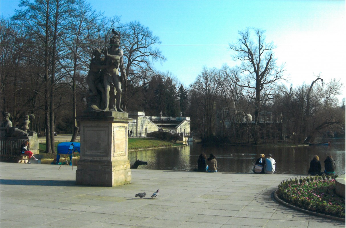 Taras Pałacu na Wyspie, na jego skraju, przy wodzie, siedzą ludzie. Na tarasie stoi rzeźba przedstawiająca kobietę i mężczyznę.