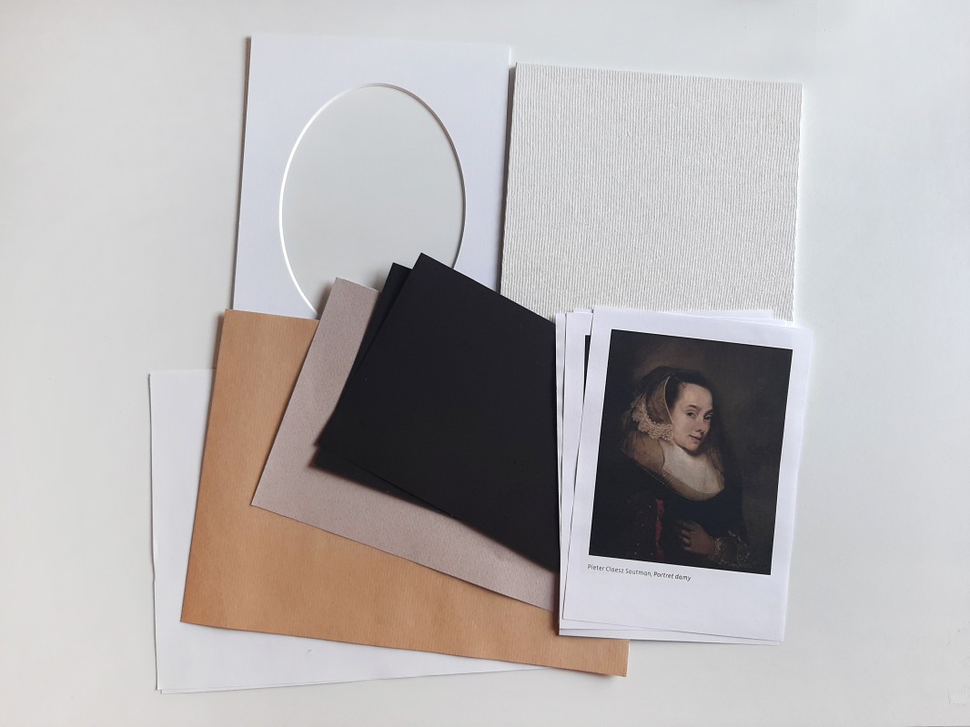 Kartki rozłożone na blacie oraz pocztówka z portretem kobiety.