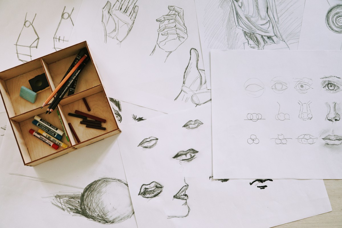 Rysunki przedstawiające usta i ręce, na rysunkach leży pudełko z kredkami. 