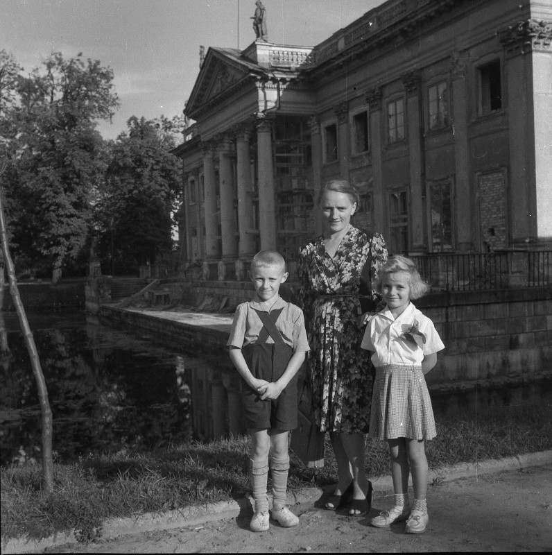 Kobieta z dwójką dzieci stoi przed Pałacem na Wyspie.
