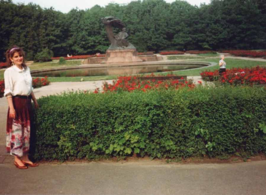 Kobieta stojąca w ogrodzie przed Pomnikiem Chopina w Łazienkach Królewskich. 