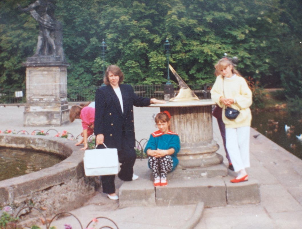 Kobieta i dwie dziewczynki przy rzeźbie przedstawiającej zegar słoneczny w Łazienkach Królewskich.