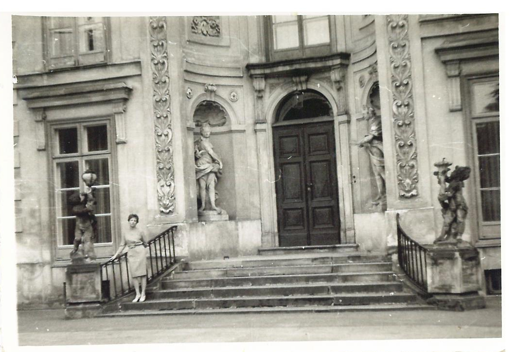 Kobieta stoi na schodach przed Pałacem Myślewickim w Łazienkach Królewskich. 