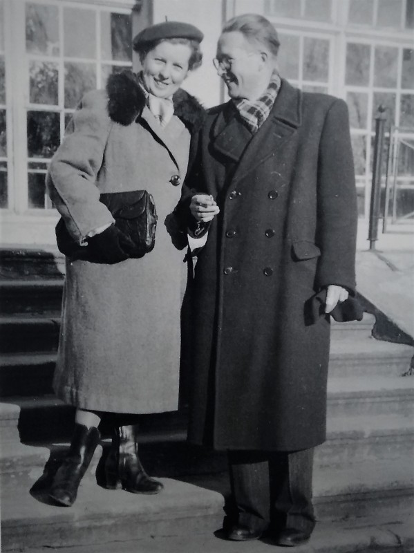 Kobieta i mężczyzna w płaszczach stoją na schodach przed Starą Oranżerią, trzymając się pod rękę. 