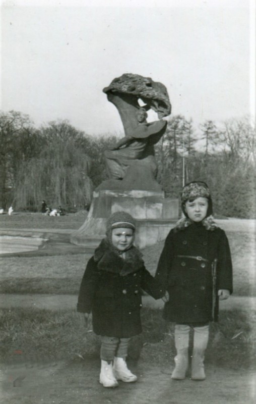 Dwóch kilkuletnich chłopców stoi przed Pomnikiem Chopina w Łazienkach Królewskich.