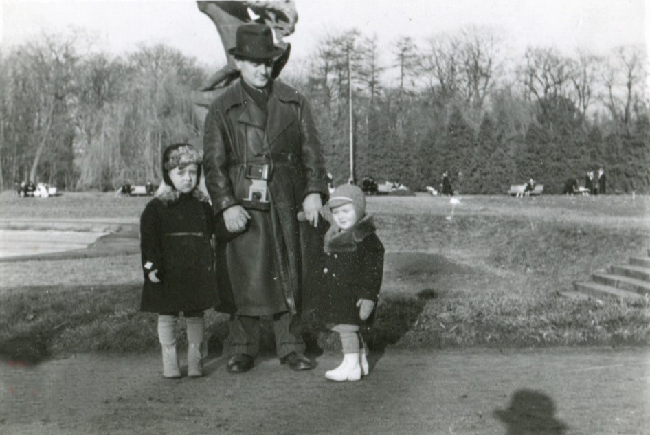 Przed Pomnikiem Chopina stoi mężczyzna, który trzyma za ręce dwóch kilkuletnich chłopców. Wszyscy mają na sobie zimowe płaszcze.