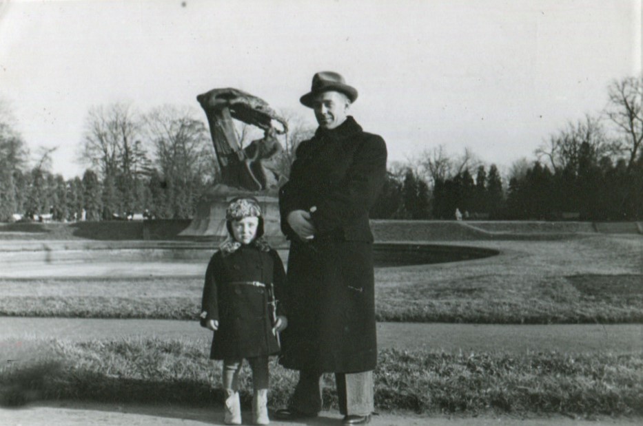Kilkuletni chłopiec i mężczyzna stoją przed Pomnikiem Chopina w Łazienkach Królewskich. Mają na sobie zimowe płaszcze, mężczyzna nosi kapelusz.
