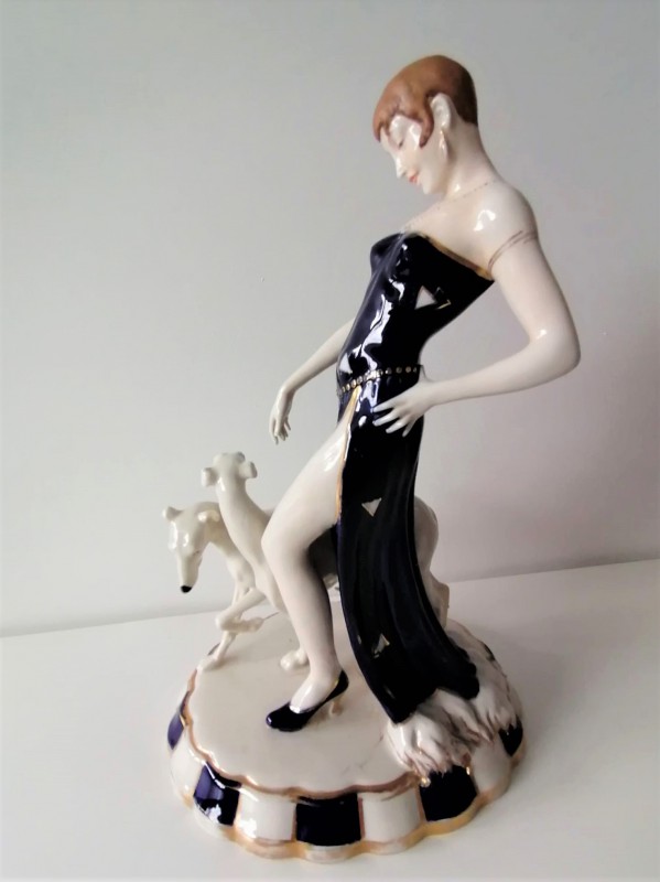 Figurka przedstawiająca kobietę w czarnej, długiej wieczorowej sukience. Obok kobiety idą dwa psy. 