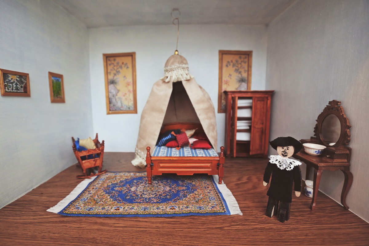 Wnętrze miniaturowego pokoju, w którym stoją łóżko i szafki. Na podłodze leży dywan, na ścianach wiszą obrazy.