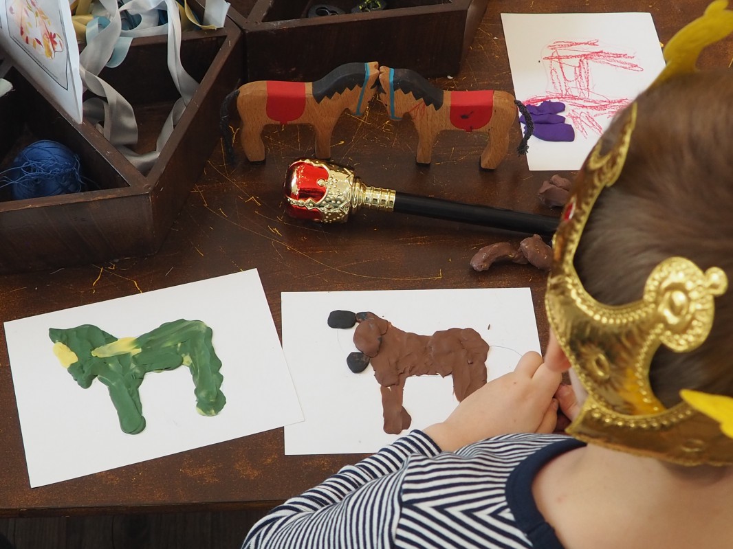 Dziecko w koronie na głowie, siedzące tyłem i patrzące na obrazki przedstawiające zwierzęta.