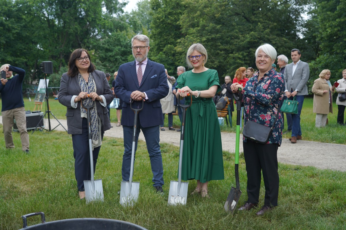 Kobieta, mężczyzna i dwie kobiety stoją w ogrodzie i trzymają przed sobą łopaty.