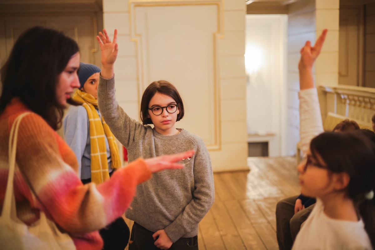 Kobieta i grupa dzieci stoją w pomieszczeniu.