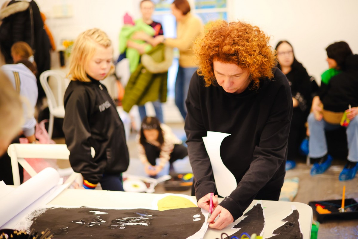 Kobieta wycina z papieru, obok stoi małe dziecko. 