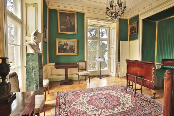 Sypialnia księcia Józefa Poniatowskiego, po lewej stronie stoi łóżko, pośrodku leży dywan, po lewej stronie stoją komody i krzesła, znajduje sie też okno, środkową ścianę zdobią obrazy i okno.