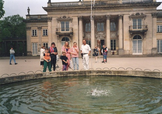 Grupa osób stoi przy fontannie przed Pałacem na Wyspie.
