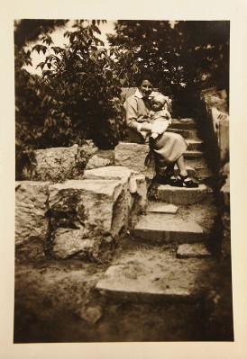 Kobieta siedząca na schodach trzyma na kolanach małe dziecko. 