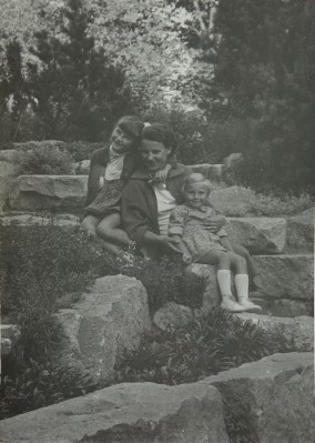 Kobieta i dwoje dzieci siedzą na kamiennych schodach w ogródku. 