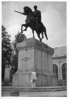 Dziewczynka stojąca pod pomnikiem przedstawiającym jeźdzca na koniu z uniesionym mieczem.