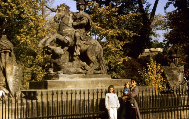 Kobieta z dwójką dzieci przed pomnikiem przedstawiającym jeźdźca na koniu. 