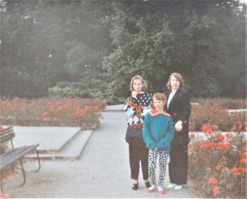 Kobieta z dwiema dziewczynkami stoi na parkowej alejce w Łazienkach Królewskich.