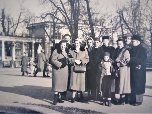 Archiwalne zdjęcie przedstawiające grupę kobiet i mężczyzn w zimowych płaszczach, którzy stoją przed pawilonem w Łazienkach Królewskich.