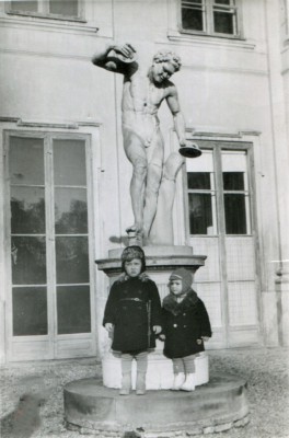 Dwóch kilkuletnich chłopców stoi pod rzeźbą na tle fasady Pałacu na Wyspie.