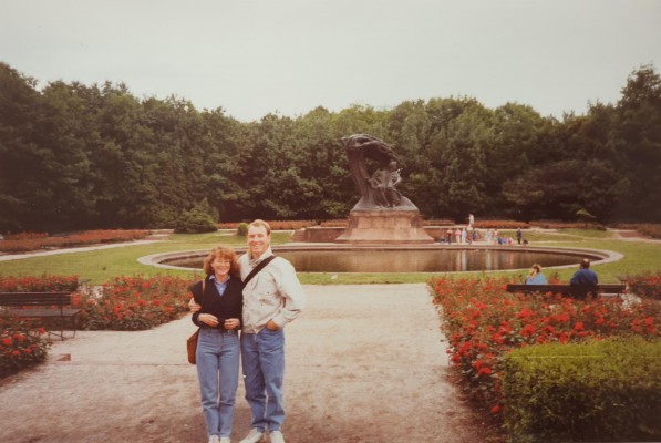 Kobieta i mężczyna stoją na tle Pomnika Chopina w Łazienkach Królewskich. 