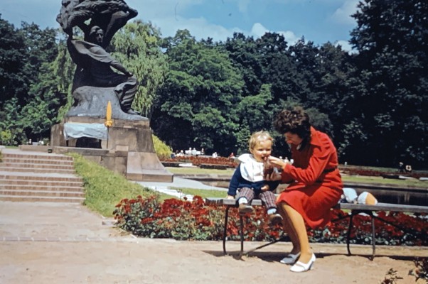 Dziecko i kobieta siedzą na ławce w parku, w tle widać Pomnik Fryderyka Chopina.