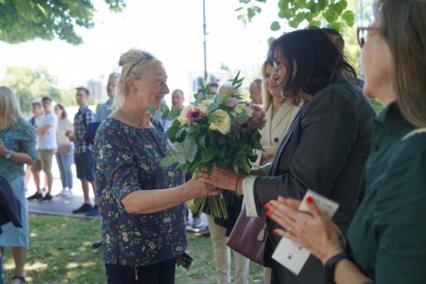 Kobieta wręcza innej kobiecie bukiet kwiatów.