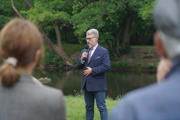 Mężczyzna w garniturze stoi na trawniku z mikrofonem w ręku. 