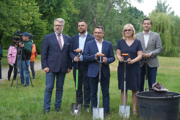 Czterech mężczyzn i kobieta stoją w ogrodzie i trzymają przed sobą łopaty.