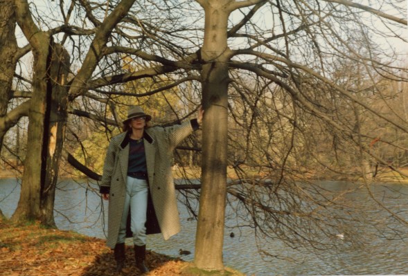 Kobieta w parku, stoi oparta o drzewo. 