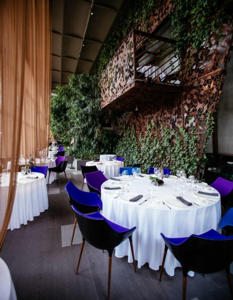Wnętrze restauracji, w której stoją okrągłe stoły nakryte białymi obrusami, wokół nich ustawione zostały niebieskie krzesła.
