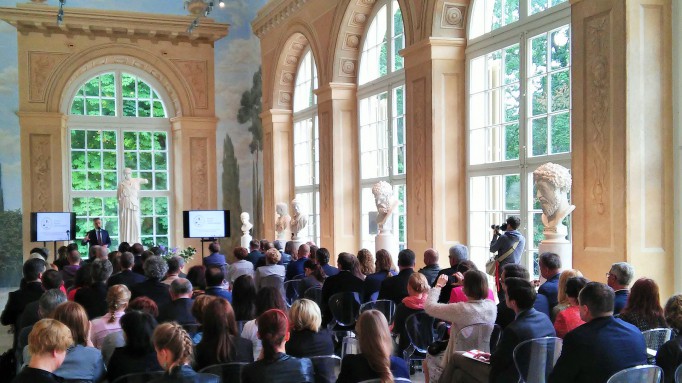 Konferencja prasowa w Starej Oranżerii, tłum osób zebrany w pomieszczeniu siedzi na krzesłach.