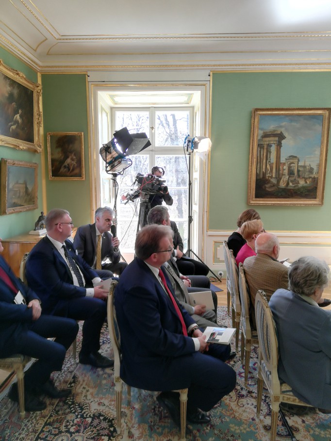 Ludzie siedzą na krzesłach w sali Pałacu Myślewickiego. 
