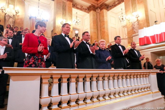 Ludzie stoją w loży teatralnej i klaszczą w dłonie.