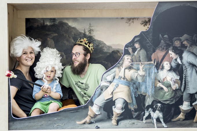 Kobieta w peruce, dziecko w peruce i mężczyzna w koronie na tle obrazu pozują do zdjęcia.
