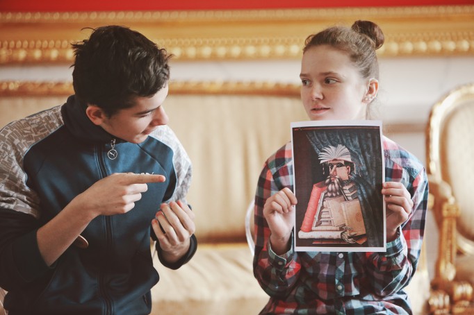 Dziewczynka trzyma obrazek, chłopiec siedzący z boku wskazuje na obrazek placem.