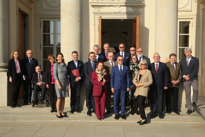 Grupa osób stoi na schodach przed Pałacem na Wyspie i pozuje do zdjęcia.