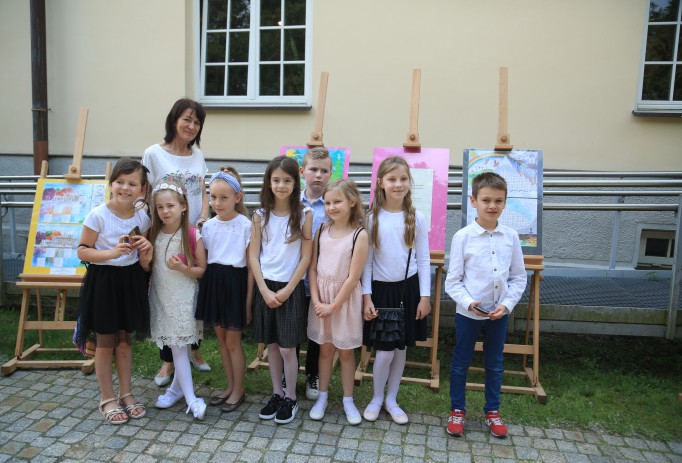 Uczniowie ubrani w biało-czarne galowe stroje pozują wraz z nauczycielką do zdjęcia.