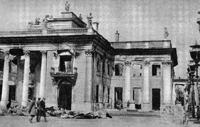 Biało-czarna fotografia Pałacu na Wyspie z czasów II wojny światowej, ukazująca zniszczenia budynku. Przed budynkiem stoją trzy osoby.
